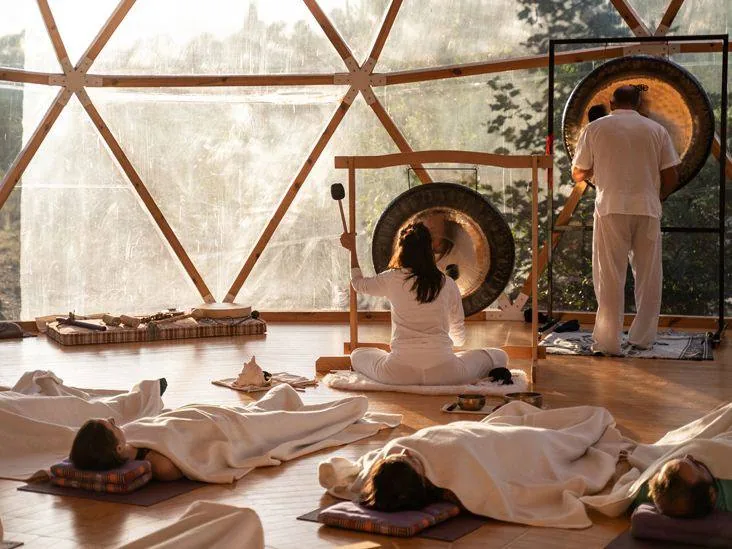 Группа людей на ковриках медитирует и отдыхает в зале с гонгом и поющими чашами