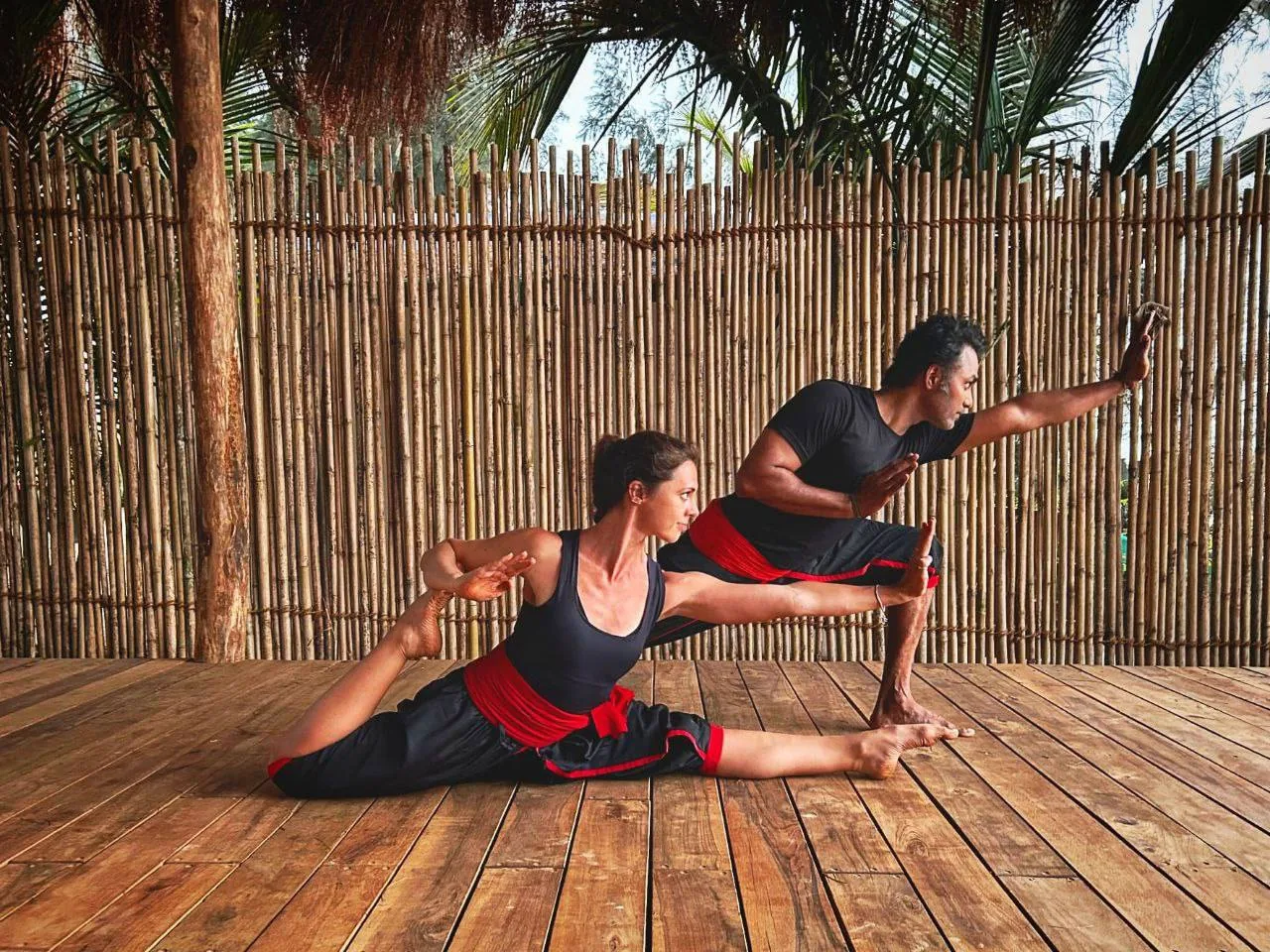 Мужчина и женщина в спортивной одежде выполняют позу йоги на деревянной площадке на улице