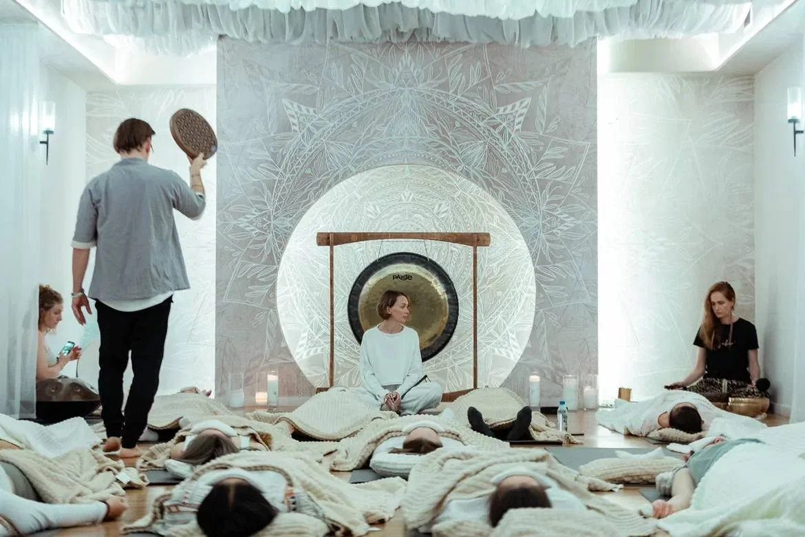 Групповая сессия гонг-медитации в студии: ведущий у гонга, участники лежат на ковриках Групповая сессия гонг-медитации в студии: ведущий у гонга, участники лежат на ковриках