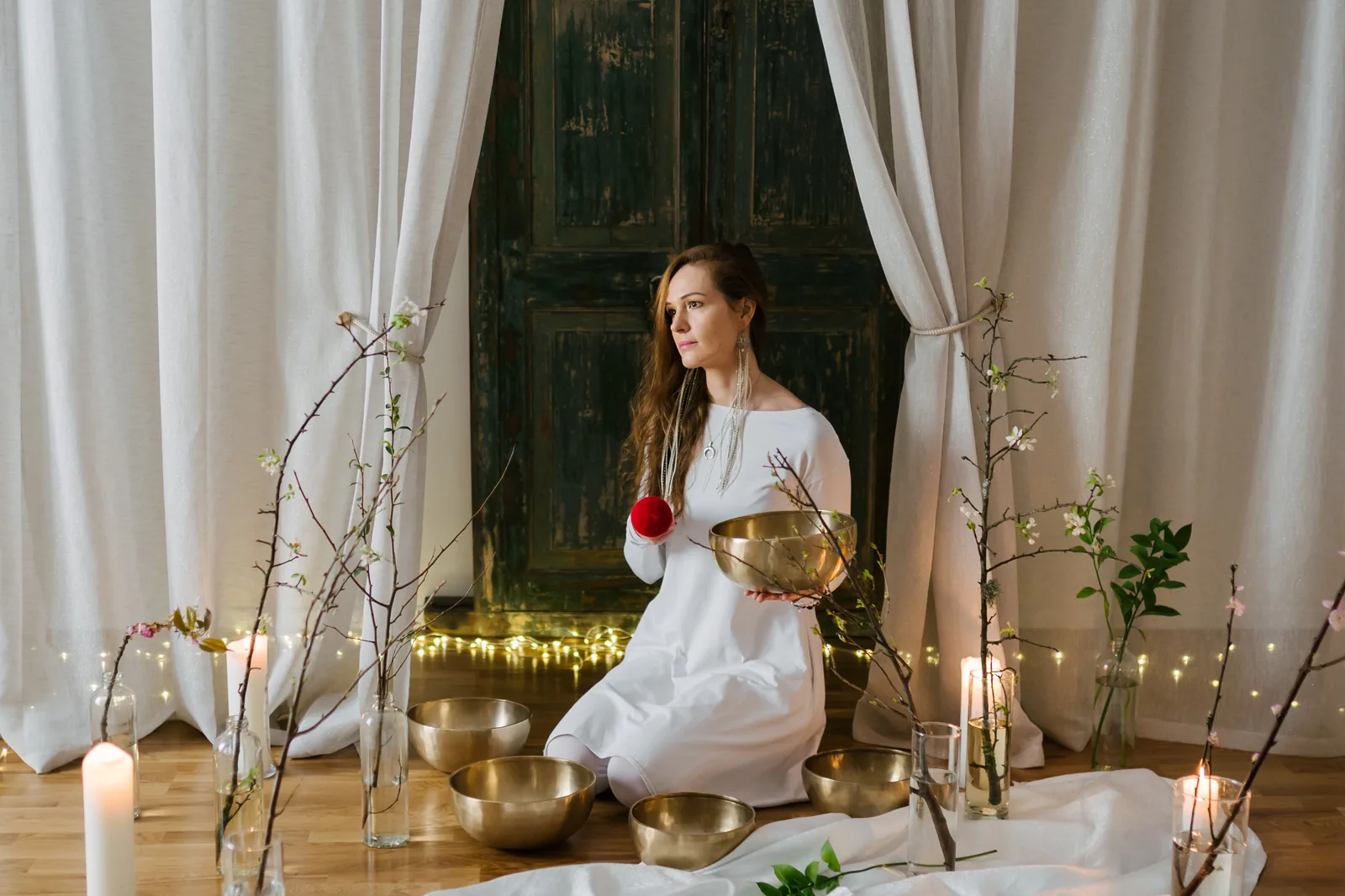Женщина в белом платье проводит расслабляющую практику с поющими чашами в студии