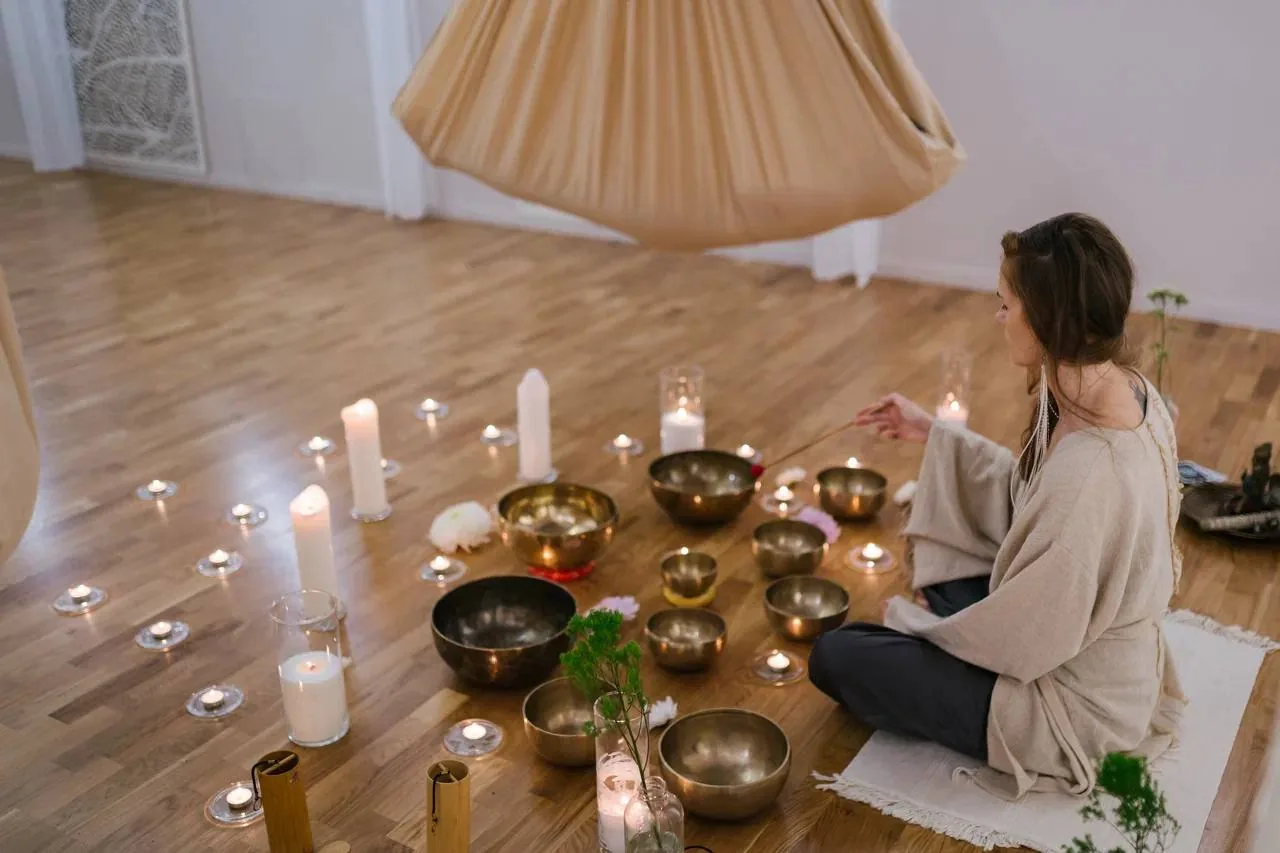 Женщина сидит на полу среди поющих чаш и свечей в тихом уединённом пространстве для расслабления